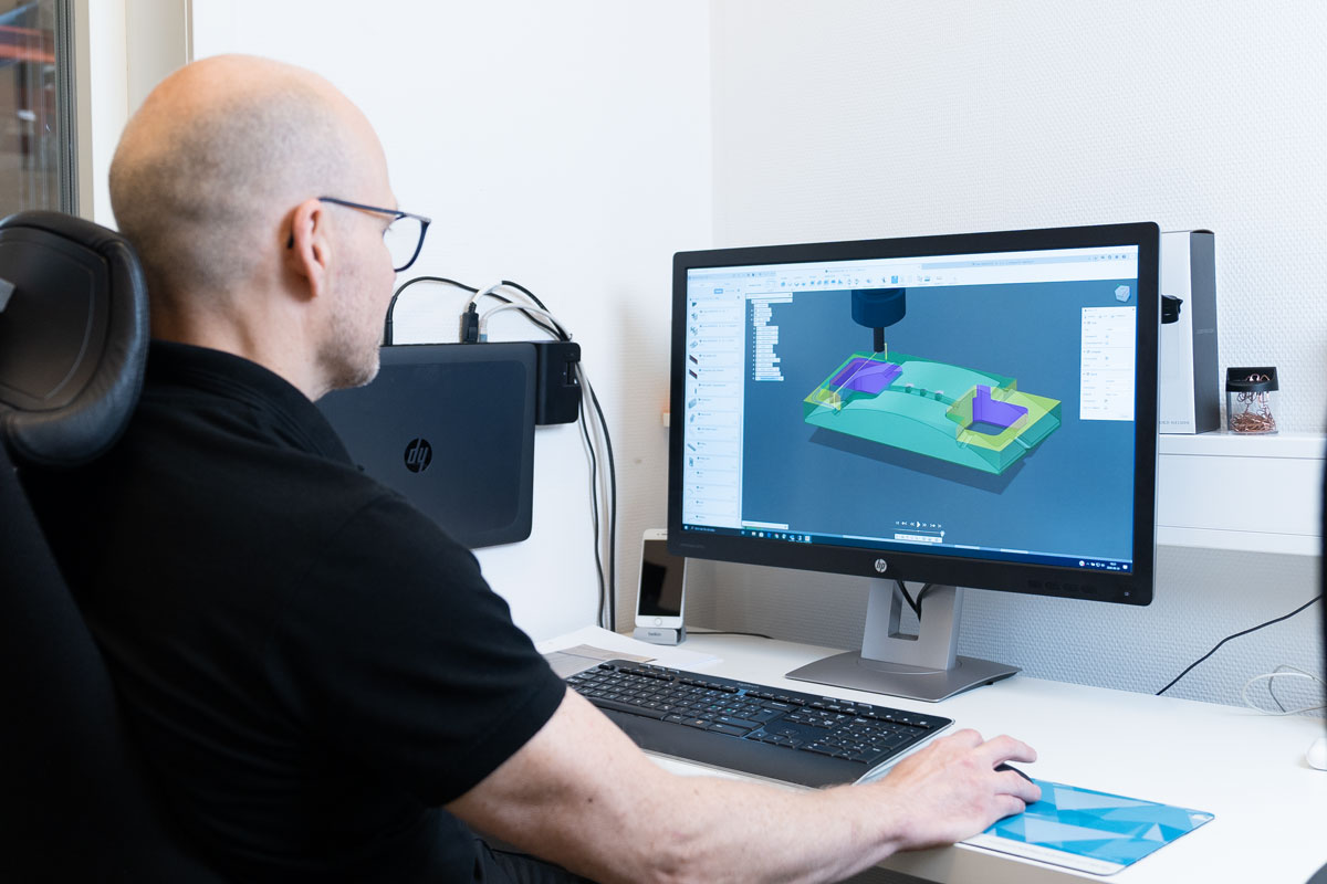Ingenjör arbetar med CAD-modell av mekanisk komponent på skärm i verkstadsmiljö